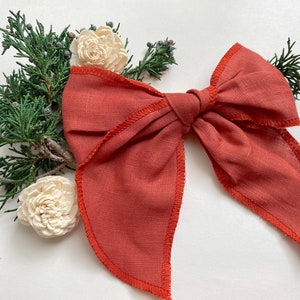 May include: A large, rust-colored fabric bow with a slightly frayed edge. The bow is tied in a classic shape with a center knot.