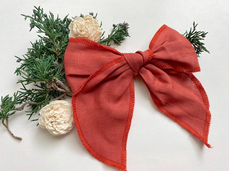 May include: A large, rust-colored fabric bow with a slightly frayed edge. The bow is tied in a classic shape with a center knot.