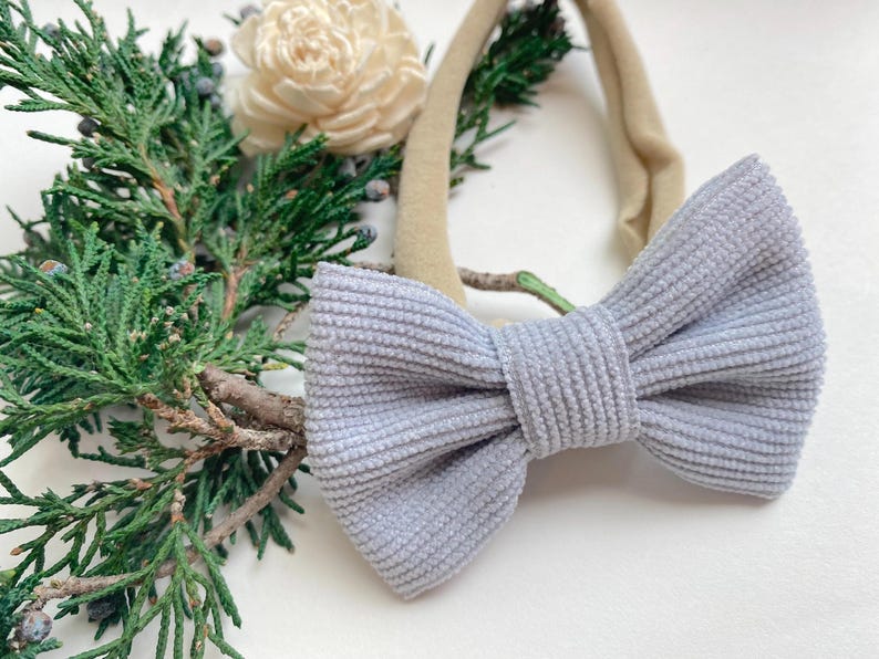 Puede incluir: Un lazo de pana gris claro atado a una diadema el&aacute;stica de color nude. La diadema es perfecta para beb&eacute;s y ni&ntilde;os peque&ntilde;os.