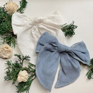 May include: Two fabric hair bows, one white and one light blue, tied in a bow shape. The bows are made of a soft, textured fabric and are perfect for adding a touch of elegance to any outfit.
