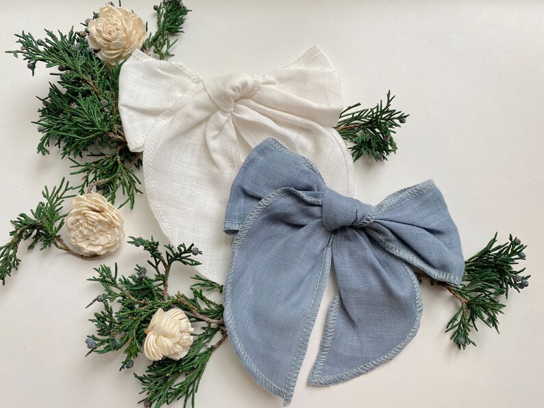 May include: Two fabric hair bows, one white and one light blue, tied in a bow shape. The bows are made of a soft, textured fabric and are perfect for adding a touch of elegance to any outfit.