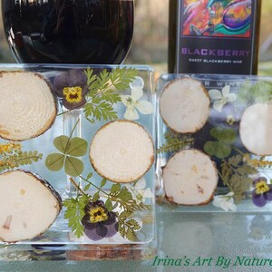 May include: Two square resin coasters featuring pressed flowers and wood slices. The coasters showcase a variety of flowers, including violets, clover, and ferns. The coasters are clear, allowing a detailed view of the flowers and wood slices.