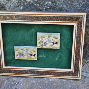 May include: Two framed miniature paintings depicting scenes of horseback riding. The paintings are set against a green velvet background and framed in a decorative ivory and gold frame.