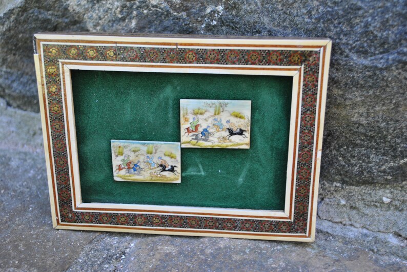May include: Two framed miniature paintings depicting scenes of horseback riding. The paintings are set against a green velvet background and framed in a decorative ivory and gold frame.