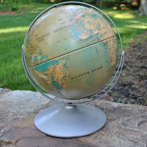 May include: A vintage globe with a silver stand. The globe is a light brown colour with blue oceans and continents in a light brown colour. The globe is labelled "Atlantic Ocean" on both sides.