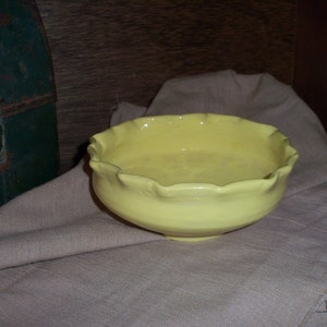 Peut inclure: Un bol en céramique jaune vif avec un bord festonné. Le bol est posé sur une surface en tissu brun clair.