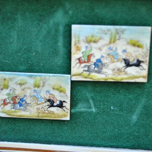 May include: Two framed miniature paintings on ivory depicting scenes of horseback riding. The paintings are set against a green background.