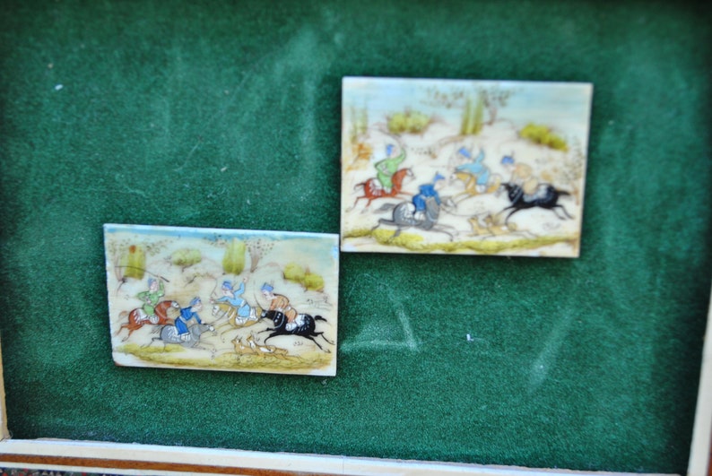 May include: Two framed miniature paintings on ivory depicting scenes of horseback riding. The paintings are set against a green background.