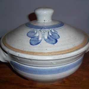 May include: A white ceramic casserole dish with a blue and brown design. The dish has a lid and two handles.