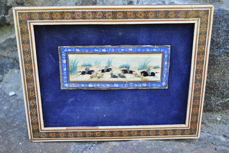 May include: A framed miniature painting depicting a scene of horseback riding. The painting is set against a blue background and features a blue, white, and gold frame with intricate floral designs.
