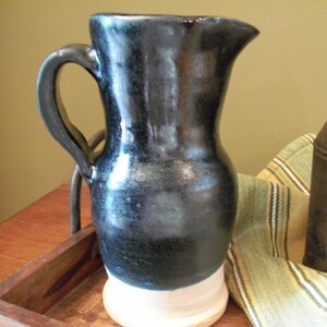 May include: A black and white ceramic pitcher with a wide mouth and a handle. The pitcher has a glossy finish and a white base.