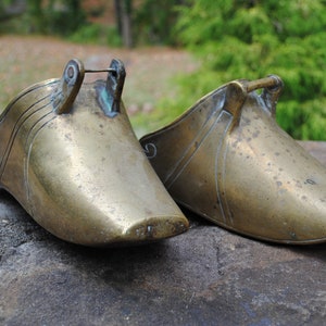 May include: Two antique brass stirrups with ornate designs. The stirrups are made of a solid brass and have a worn, aged patina.
