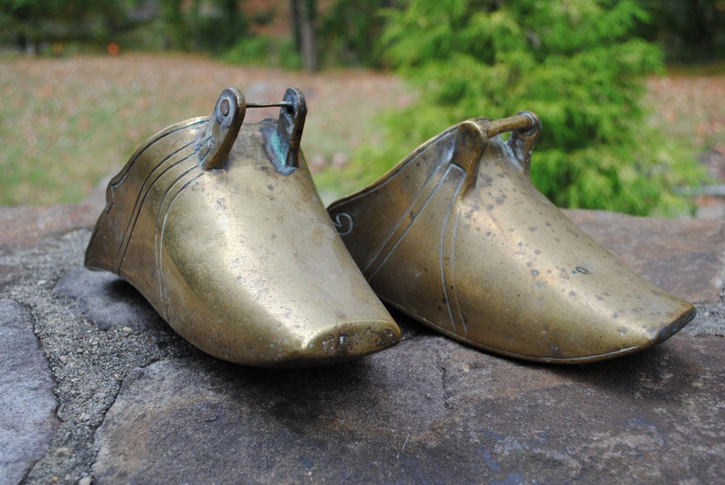 May include: Two antique brass stirrups with ornate designs. The stirrups are made of a solid brass and have a worn, aged patina.
