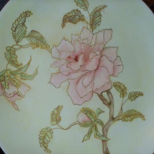 May include: A decorative plate with a floral design featuring a pink flower with gold accents and green leaves.