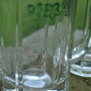 May include: Two clear glass beer mugs with handles. The mugs have a green inscription on the side.