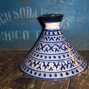 Può includere: Un coperchio per tagine in ceramica bianca con un motivo geometrico blu e bianco. Il coperchio è rotondo e ha una cima a forma di cono.