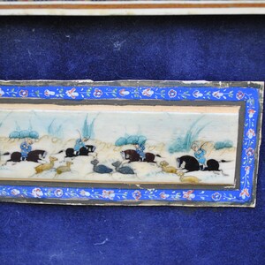 May include: A framed miniature painting on ivory depicting a hunting scene. The painting shows four figures on horseback, chasing after deer in a landscape with tall grasses. The painting is framed in a decorative border with floral motifs.