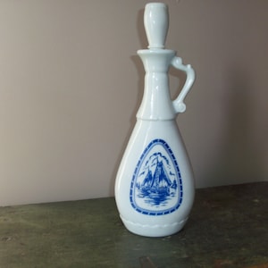Könnte beinhalten: Weiße Keramikflasche mit einem blauen und weißen Segelboot-Design. Die Flasche hat einen Stopfen und einen Griff.