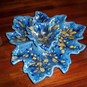 May include: A blue and yellow ceramic serving dish with three sections. The dish is shaped like a flower with wavy edges.