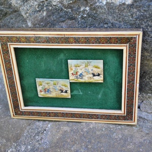May include: Two framed miniature paintings depicting scenes of horseback riding in a desert landscape. The paintings are set against a green velvet background and framed with a decorative ivory and wood frame.