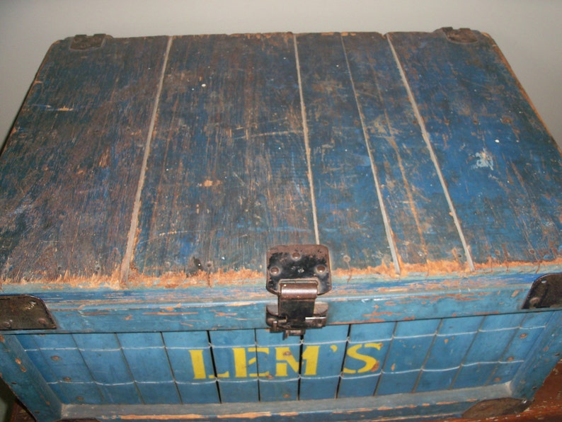 May include: A vintage wooden crate painted blue with the word "LEM'S" in yellow letters. The crate has a metal hinge and is weathered with age.
