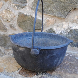 May include: A black cast iron pot with a handle. The pot is sitting on a stone surface.