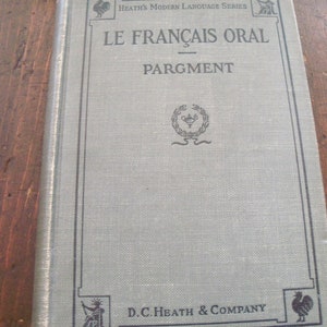 May include: A vintage book titled "Le Francais Oral" by Pargment, part of the Heath's Modern Language Series. The book cover is a light blue color with a black border and a decorative emblem in the center.