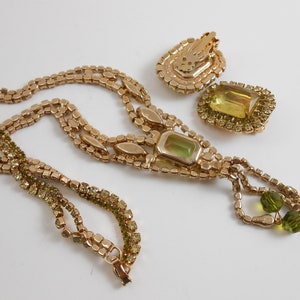 May include: A gold tone necklace and earrings set with a large green stone and smaller green rhinestones. The necklace has a tassel of green beads.