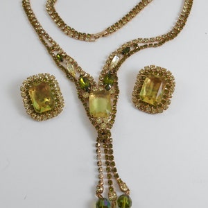 May include: A vintage green and yellow rhinestone necklace and earrings set. The necklace features a long, dangling tassel with three green beads at the end. The earrings are rectangular with a large, faceted, yellow rhinestone in the center.