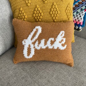 May include: Two crocheted throw pillows, one with a yellow textured surface and the other with a brown surface and the word "f*ck" embroidered in white.