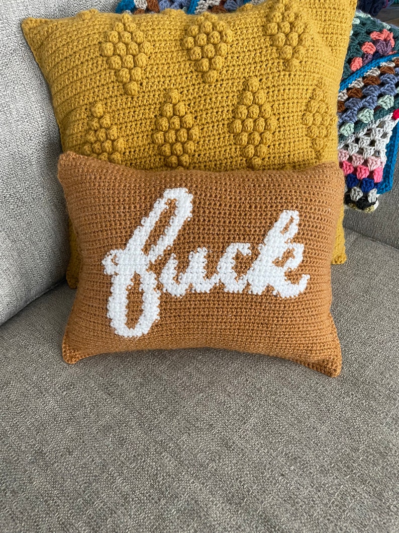May include: Two crocheted throw pillows, one with a yellow textured surface and the other with a brown surface and the word "f*ck" embroidered in white.