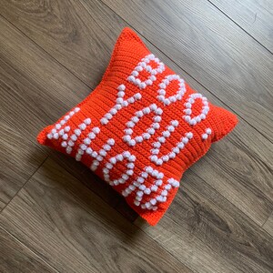 May include: Orange crocheted pillow with the word "Hello" spelled out in white yarn.