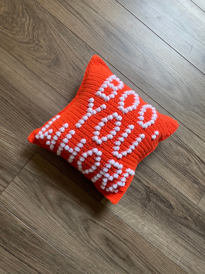 May include: Orange crocheted pillow with the word "Hello" spelled out in white yarn.