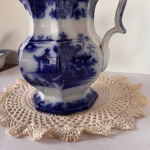 May include: A blue and white porcelain pitcher with a decorative floral and landscape design. The pitcher has a silver handle and a octagonal base.