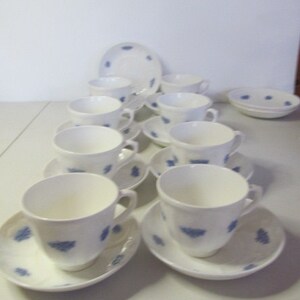 May include: A set of ten white teacups and saucers with a blue floral pattern. The cups and saucers are arranged in a pyramid shape on a white surface.