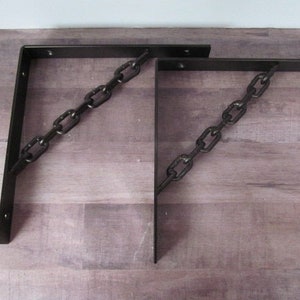 May include: Two black metal shelf brackets with a chain design. The brackets are angled and have a rustic look.