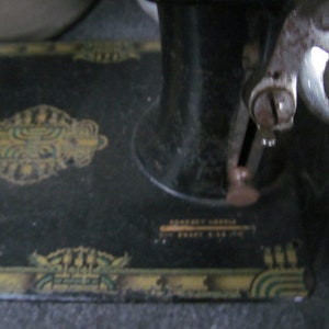 Op de afbeelding: Een zwarte vintage naaimachine met een decoratief ontwerp op de basis. De machine heeft een metalen voetpedaal en een naald.