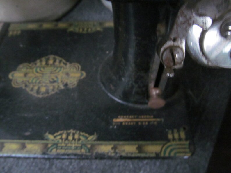 Op de afbeelding: Een zwarte vintage naaimachine met een decoratief ontwerp op de basis. De machine heeft een metalen voetpedaal en een naald.