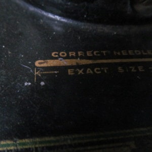 Op de afbeelding: Close-up van een zwarte naaimachine met gouden letters die "Correct Needle Exact Size" lezen.