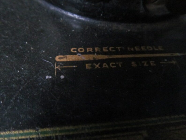 Op de afbeelding: Close-up van een zwarte naaimachine met gouden letters die "Correct Needle Exact Size" lezen.