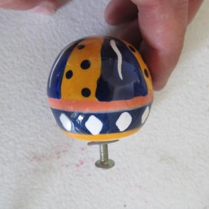 Peut inclure: Un bouton en céramique avec un motif géométrique bleu, jaune et blanc. Le bouton a une vis sur le dessous.