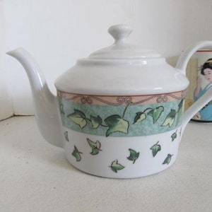 May include: White porcelain teapot with a green and brown ivy design. The teapot has a lid and a spout.