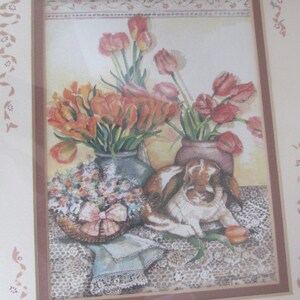 May include: A framed watercolor painting of a still life with a bouquet of orange tulips, a vase of pink tulips, and a brown rabbit sitting on a lace tablecloth.