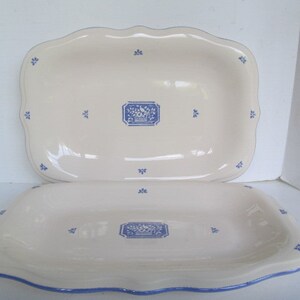 Puede incluir: Dos platos de servir de cerámica blanca con diseños florales azules. El plato más grande es rectangular con bordes festoneados. El plato más pequeño es ovalado con un borde azul.