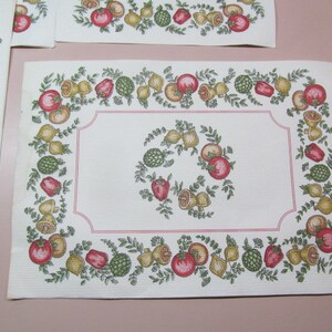 May include: White placemat with a red, green, and yellow border featuring a repeating pattern of fruit and vegetables. The border is outlined in pink.