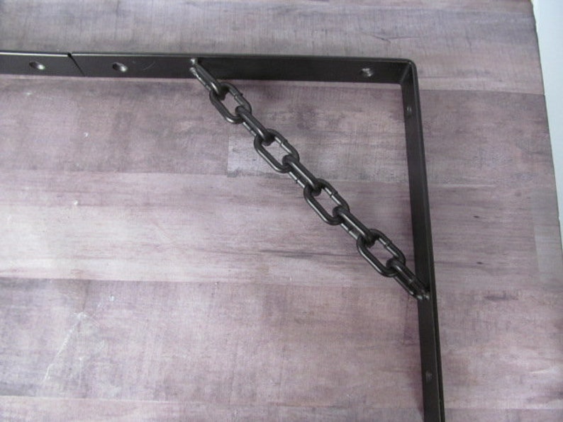 May include: Black metal shelf bracket with a black chain attached to it. The bracket is mounted to a light wood surface.