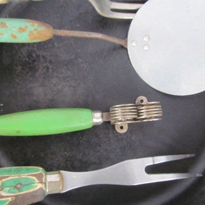 Puede incluir: Un juego de cuatro utensilios de cocina vintage con mangos verdes y blancos. Los utensilios incluyen una esp&aacute;tula, un tenedor, un cuchillo y un machacador de patatas.