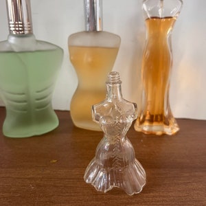 May include: Three glass perfume bottles, one clear, one light green, and one amber. The clear bottle is shaped like a woman's dress.