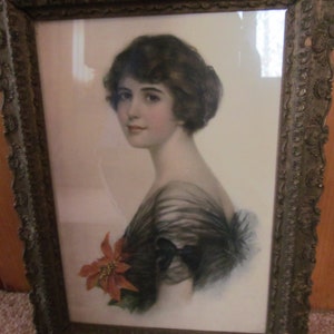 May include: A framed portrait of a woman with dark hair wearing a black dress with a red flower. The frame is ornate and has a gold finish.