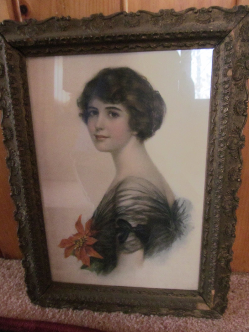 May include: A framed portrait of a woman with dark hair wearing a black dress with a red flower. The frame is ornate and has a gold finish.